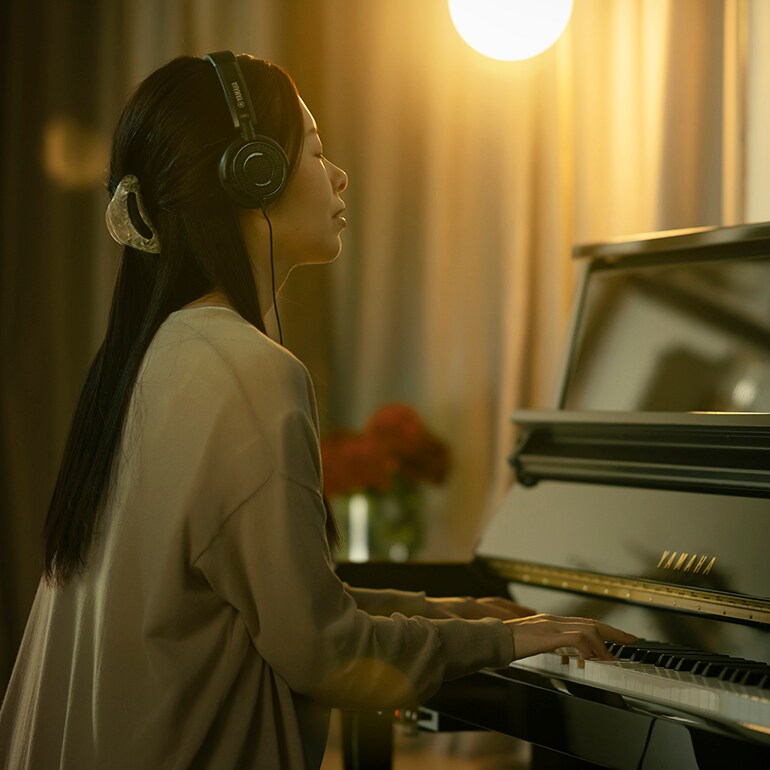 A woman enjoys playing the piano while wearing headphones