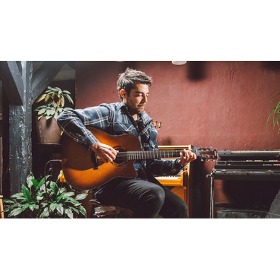 Man sitting by a piano and playing the TAG3 C acoustic guitar.
