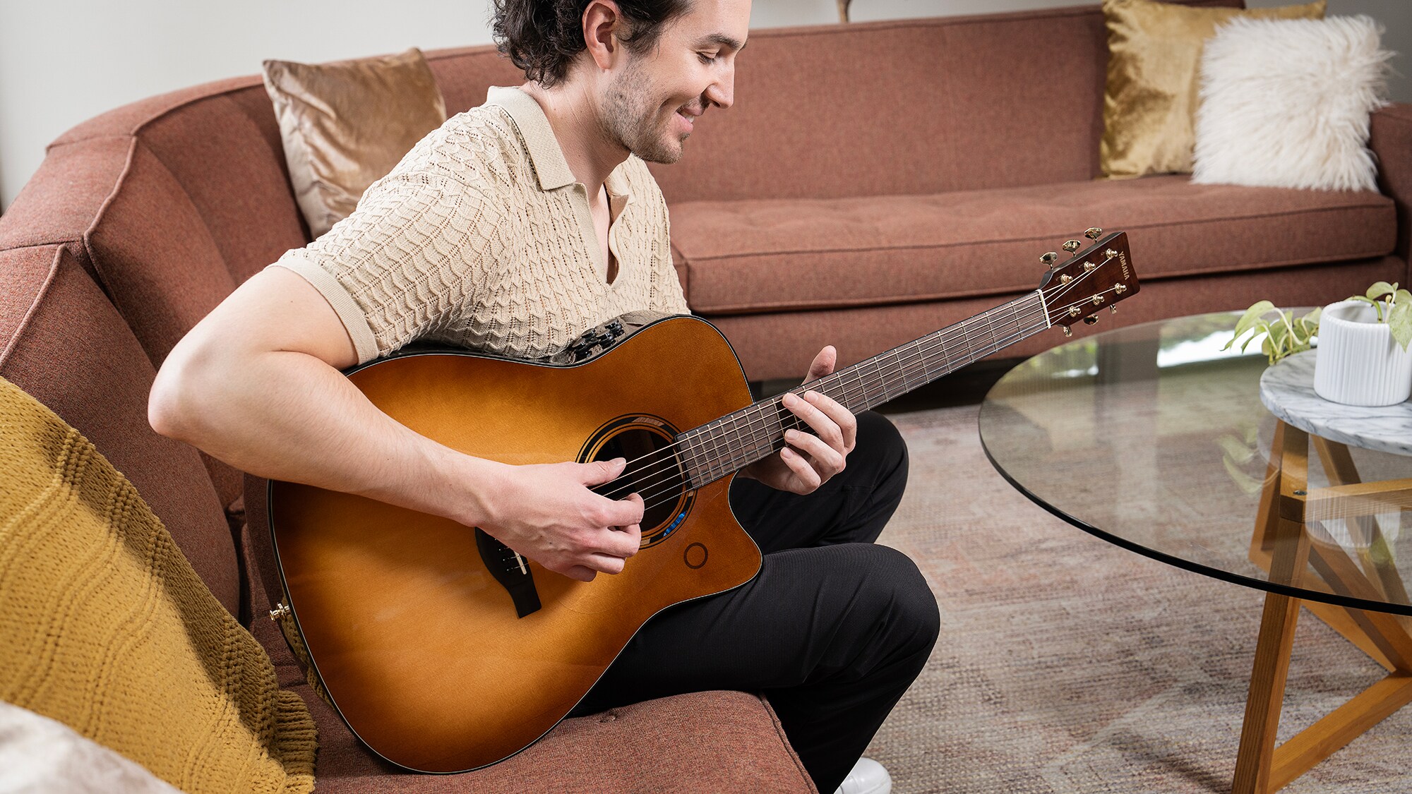 A man sitting on a sofa in the living room playing an TAG3 C acoustic guitar