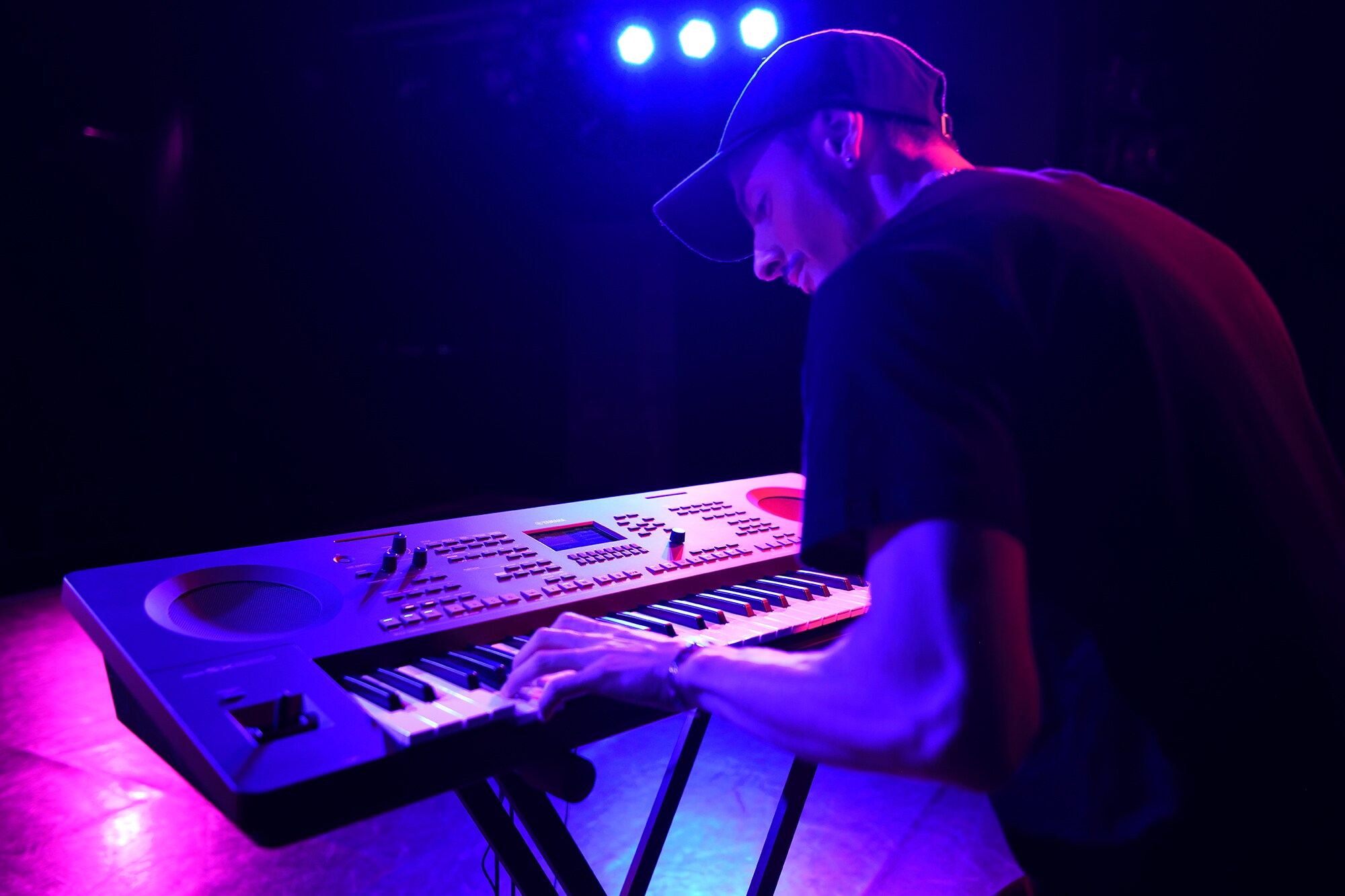 ภาพคนกำลังเล่น Arranger Workstation ของ Yamaha บนขาตั้งอยู่ใต้แสงไฟเวที