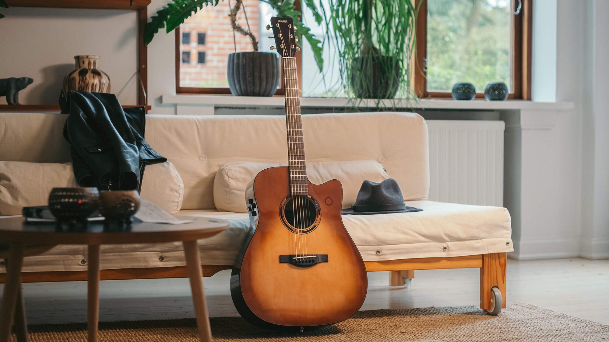 ภาพกีตาร์โปร่งรุ่น TAG3 C วางอยู่บนโซฟา โดยมีกระเป๋าวางอยู่ข้างๆ