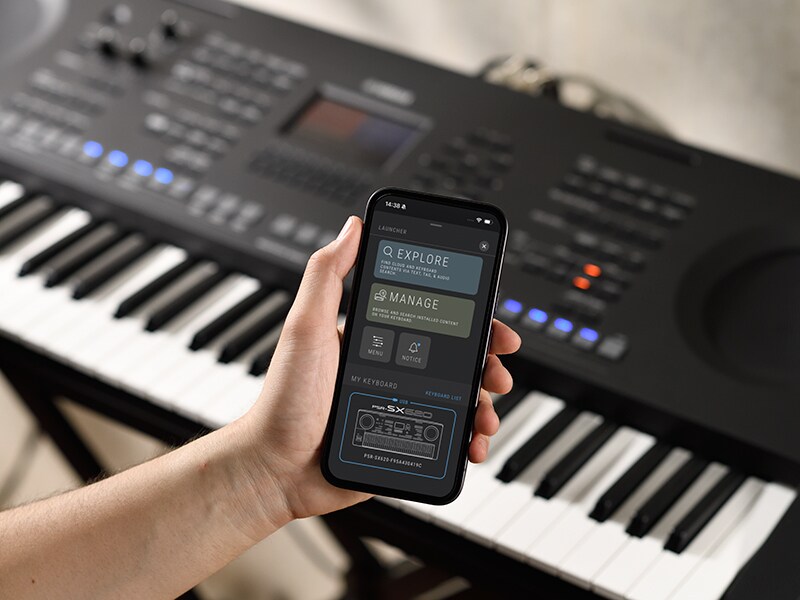 ภาพ PSR-SX920 ของ Yamaha และภาพมือที่กำลังถือสมาร์ทโฟนพร้อมหน้าจอเครื่องเล่นเพลง