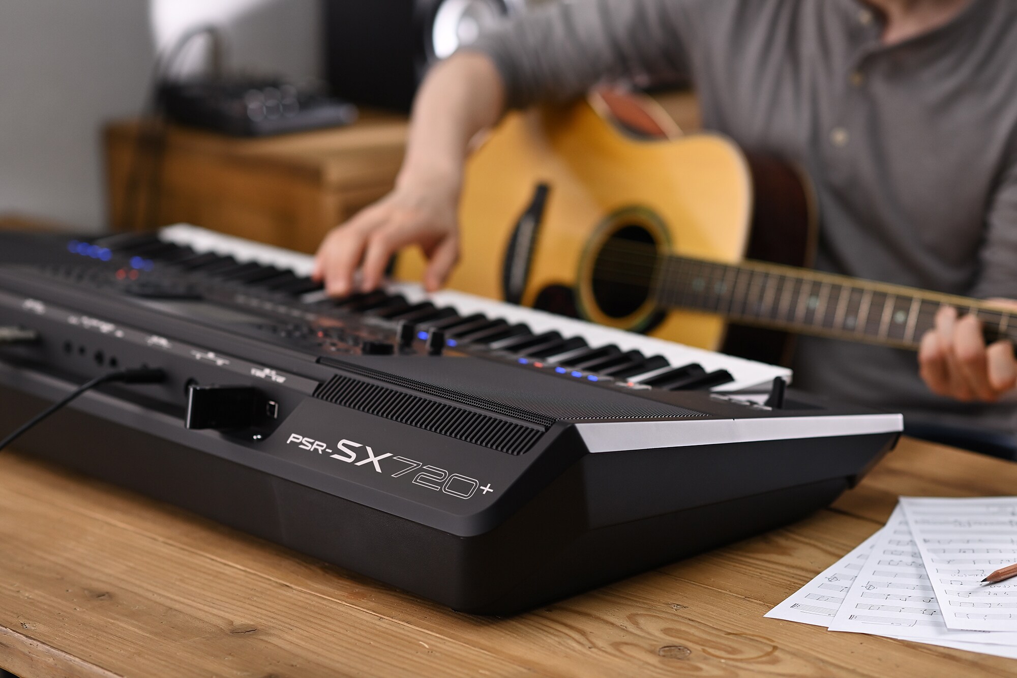 ภาพบุคคลหนึ่งกำลังเล่น Arranger Workstation PSR-SX720+ ของ Yamaha ขณะถือกีตาร์อยู่ในมือ